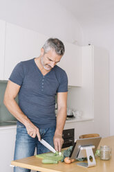 Mature man in kitchen cutting vegetables and looking at tablet - ALBF00251