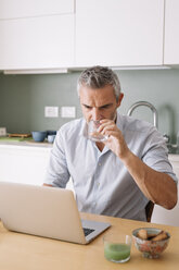 Man drinking water from glass and using laptop in home office - ALBF00255