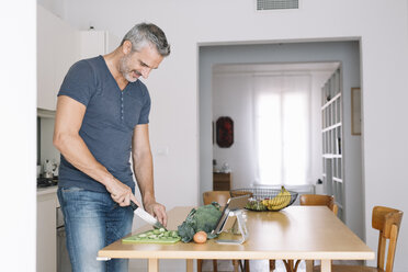 Mature man in kitchen cutting vegetables and looking at tablet - ALBF00266