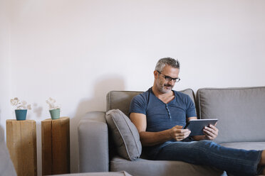 Älterer Mann sitzt zu Hause auf der Couch und benutzt ein Tablet - ALBF00272