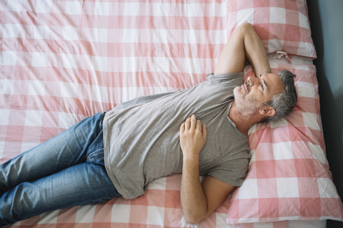 Entspannter reifer Mann auf dem Bett liegend, lizenzfreies Stockfoto