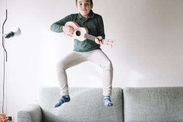Porträt eines Jungen mit Ukulele, der auf der Couch in die Luft springt - ALBF00290