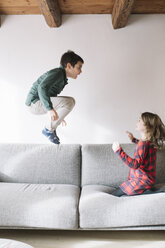 Junge, der auf der Couch in die Luft springt, während seine Schwester ihn beobachtet - ALBF00291
