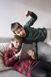 Mädchen liegt auf der Couch im Wohnzimmer und benutzt ein Tablet, während ihr Bruder sie unterbricht - ALBF00302