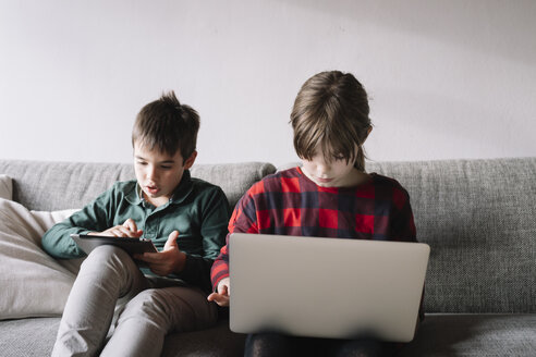 Brother and sister sitting on the couch in the living room using mobile devices - ALBF00303