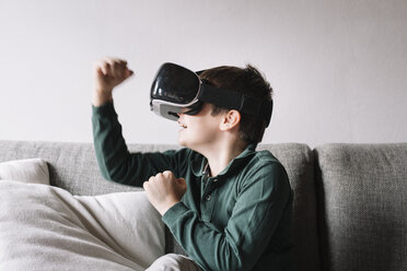 Junge sitzt auf der Couch im Wohnzimmer und benutzt eine Virtual-Reality-Brille - ALBF00306