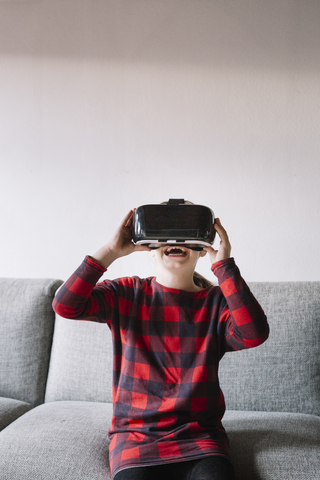 Girl sitting on the couch in the living room using Virtual Reality Glasses stock photo