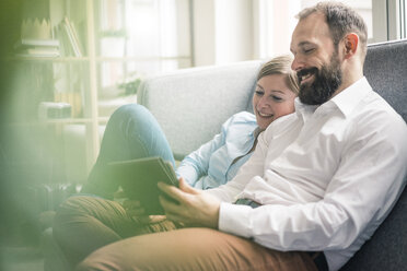 Smiling couple using tablet on couch - JOSF01907