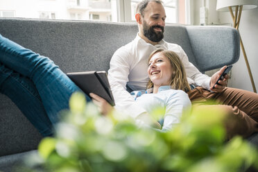 Smiling couple using tablet and cell phone on couch - JOSF01908