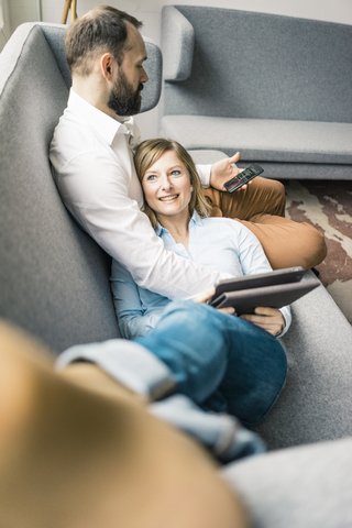Smiling woman with tablet and man with cell phone on couch stock photo