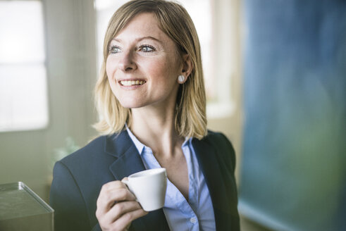 Smiling businesswoman holding espresso cup in office - JOSF01915