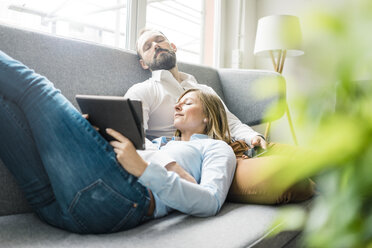 Couple relaxing on couch with tablet and cell phone - JOSF01916