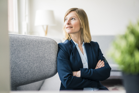 Lächelnde Geschäftsfrau sitzt auf der Couch in der Büro-Lounge, lizenzfreies Stockfoto