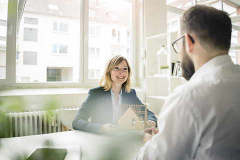 Frau mit Hausmodell lächelt Mann im Büro an, lizenzfreies Stockfoto