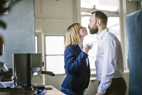 Businessman kissing businesswoman in office stock photo