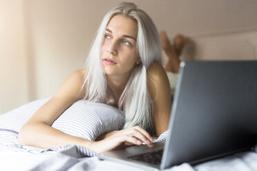 Junge Frau im Bett liegend mit Laptop - GIOF03497