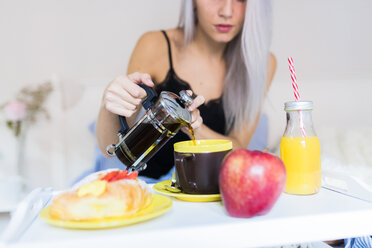 Junge Frau frühstückt im Bett und gießt Kaffee in eine Tasse - GIOF03502