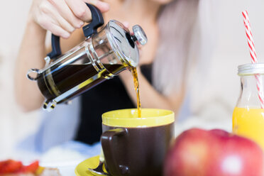 Junge Frau frühstückt im Bett und gießt Kaffee in eine Tasse - GIOF03503