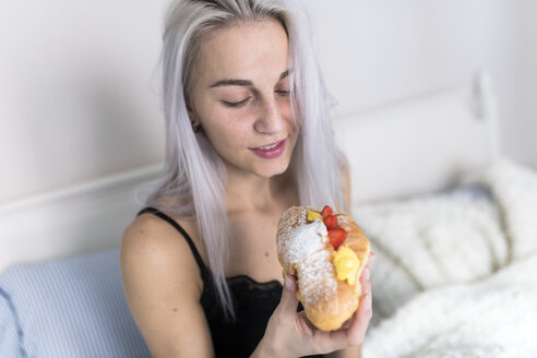 Junge Frau genießt ein süßes Croissant im Bett - GIOF03505