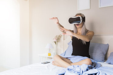 Junge Frau sitzt im Bett und trägt eine VR-Brille - GIOF03510
