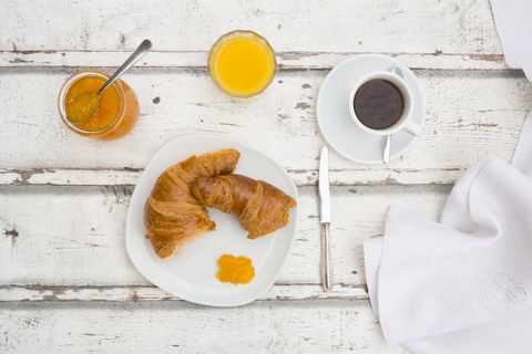 Croissant-Frühstück, Aprikosenmarmelade, Tasse Kaffee und Orangensaft, lizenzfreies Stockfoto
