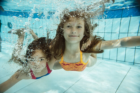 Porträt von zwei Mädchen, die im Schwimmbad unter Wasser schwimmen - MFF04170