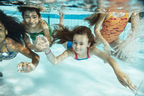 Porträt von glücklichen Kindern, die im Schwimmbad unter Wasser schwimmen, lizenzfreies Stockfoto