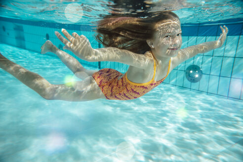 Porträt eines lächelnden Mädchens, das im Schwimmbad unter Wasser schwimmt - MFF04176