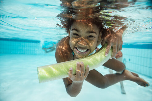 Porträt eines lächelnden Mädchens mit Poolnudel unter Wasser im Schwimmbad - MFF04180