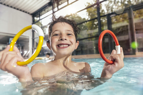 Porträt eines stolzen Jungen, der zwei Tauchringe im Schwimmbad hält - MFF04183