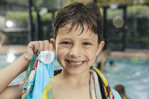 Porträt eines stolzen Jungen, der sein Schwimmabzeichen am Beckenrand eines Hallenbades zeigt - MFF04216