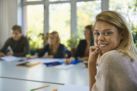 Porträt eines lächelnden Studenten, der an einem Tisch in der Universität sitzt, lizenzfreies Stockfoto