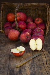 Red apples in basket, knife and halved on wood - LVF06428