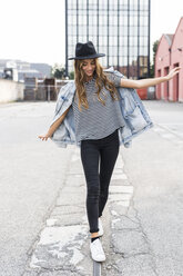 Fashionable young woman wearing hat balancing on rail - GIOF03524