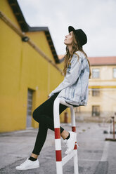 Fashionable young woman wearing hat sitting on railing - GIOF03530