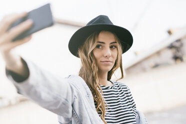 Porträt einer modischen jungen Frau mit Hut, die ein Selfie mit ihrem Smartphone macht - GIOF03532