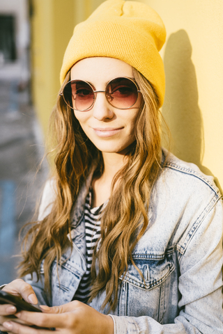 Porträt einer modischen jungen Frau mit gelber Kappe und Sonnenbrille, lizenzfreies Stockfoto