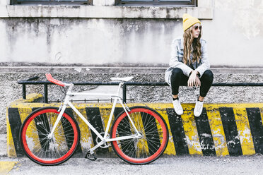 Modische junge Frau mit Fahrrad auf Geländer sitzend - GIOF03548