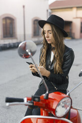 Portrait of fashionable young woman with red motor scooter using cell phone - GIOF03557