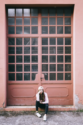 Modische junge Frau sitzt vor dem Eingangstor, lizenzfreies Stockfoto