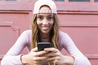 Portrait of fashionable young woman with cell phone wearing basecap - GIOF03566