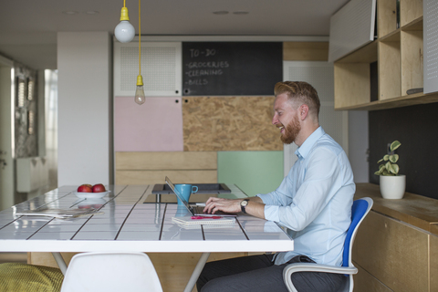 Lachender Freiberufler, der zu Hause an seinem Laptop arbeitet, lizenzfreies Stockfoto