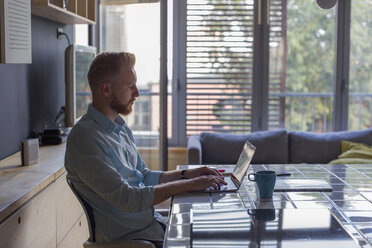 Freelance businessman working on his laptop at home - MOMF00314