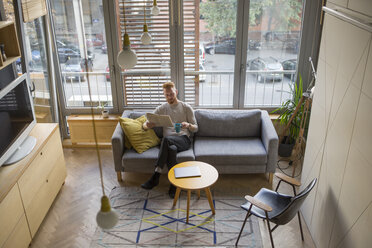 Man drinking coffee and reading newspaper in his living room - MOMF00318