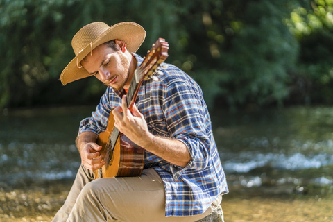 Mann spielt Gitarre am Flussufer, lizenzfreies Stockfoto