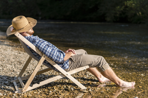 Mann entspannt im Strandkorb am Flussufer, lizenzfreies Stockfoto