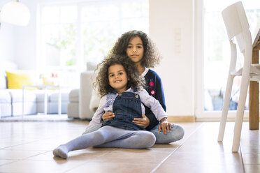 Kleines Mädchen sitzt auf dem Boden im Wohnzimmer und hält ihre Schwester, Porträt - MOEF00295