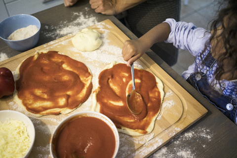 Mädchen in der Küche, das lernt, wie man eine Pizza backt und Tomatensauce aufträgt, lizenzfreies Stockfoto