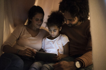 Eltern sitzen mit ihrer Tochter im Kinderzimmer und schauen auf ein digitales Tablet - MOEF00301