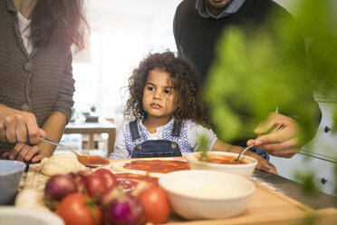 Family baking pizza in kitchen, daughter spreading tomato sauce - MOEF00305